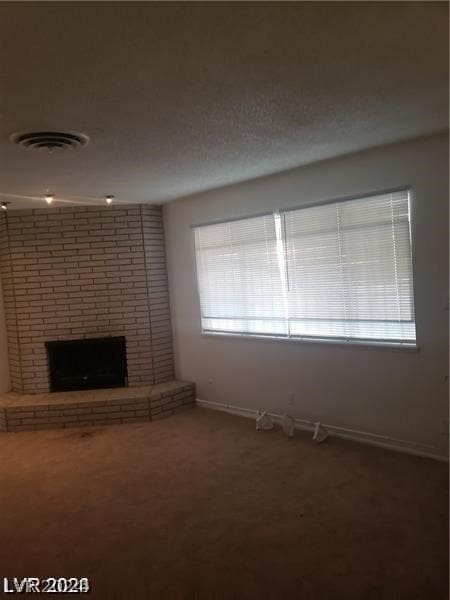 unfurnished living room with brick wall, a fireplace, carpet floors, and a textured ceiling