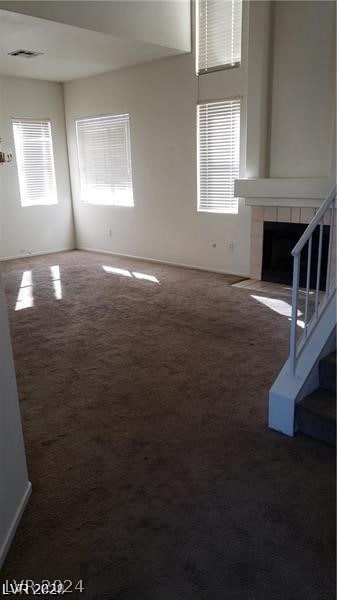 unfurnished living room featuring a tile fireplace and dark colored carpet