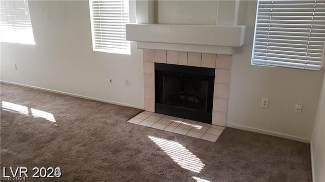 unfurnished living room with a tile fireplace, light colored carpet, and a healthy amount of sunlight