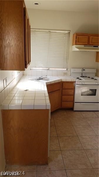 kitchen with light tile flooring, sink, tile countertops, and white range with gas cooktop