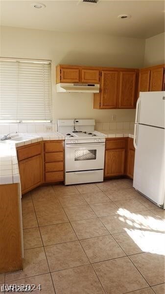 kitchen featuring light tile floors, tile counters, sink, and white appliances