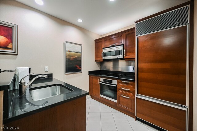 kitchen with appliances with stainless steel finishes, dark stone countertops, light tile floors, and sink