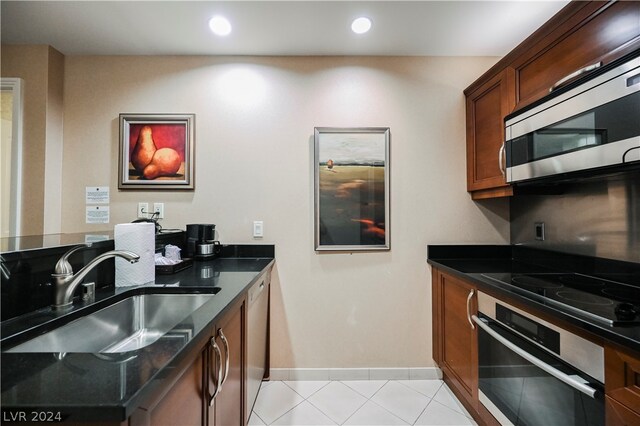 kitchen featuring appliances with stainless steel finishes, dark stone countertops, light tile floors, and sink