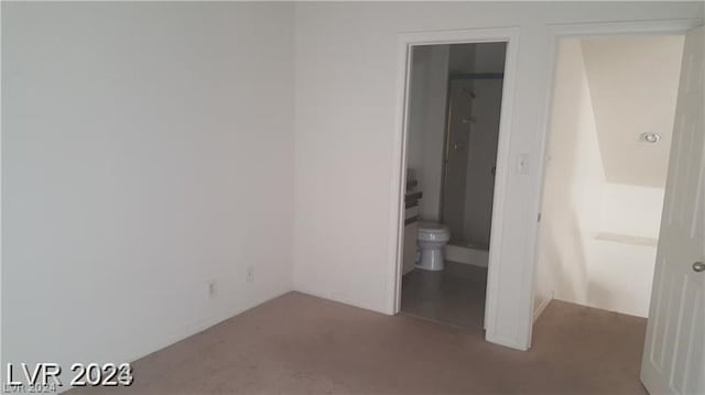 unfurnished bedroom featuring ensuite bath and dark colored carpet