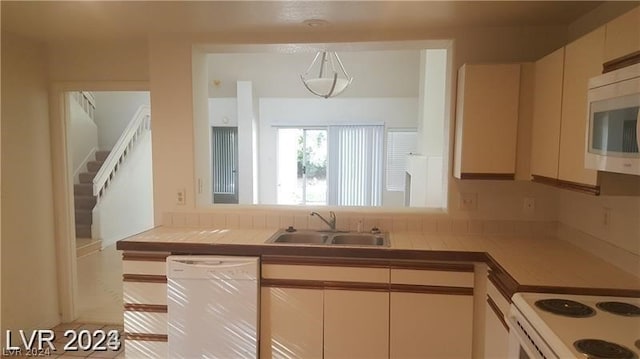 kitchen with stainless steel microwave, range, sink, white dishwasher, and tile counters