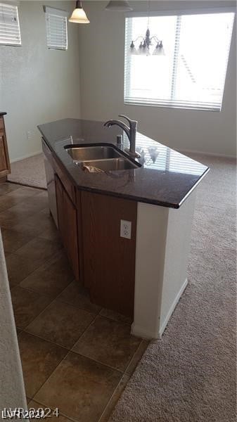 kitchen featuring carpet flooring, sink, an island with sink, and pendant lighting