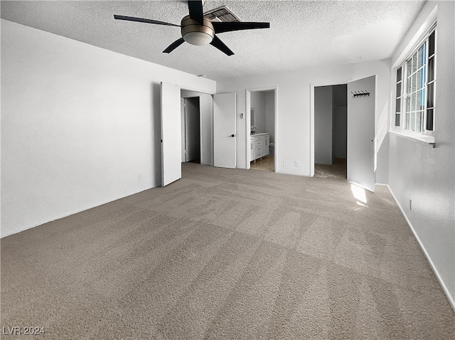 unfurnished bedroom featuring ceiling fan, carpet, connected bathroom, and a textured ceiling