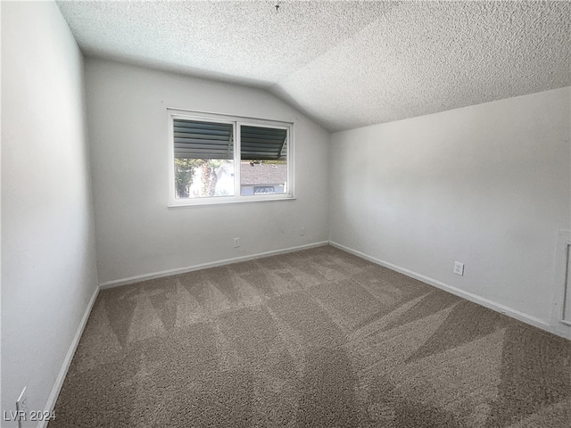 empty room featuring vaulted ceiling, a textured ceiling, and carpet flooring