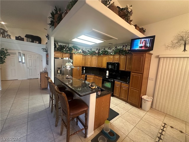 kitchen with an island with sink, stove, stainless steel fridge with ice dispenser, and light tile floors