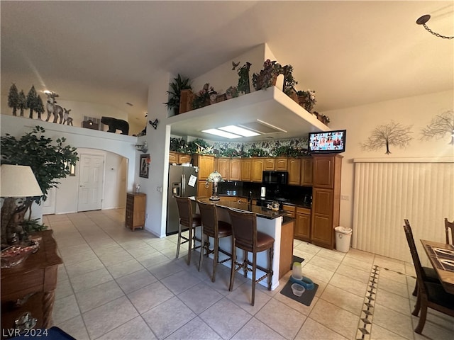 kitchen with vaulted ceiling, stainless steel fridge with ice dispenser, light tile flooring, a kitchen island, and a breakfast bar area