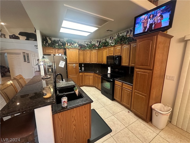 kitchen with backsplash, a center island with sink, black appliances, sink, and light tile floors