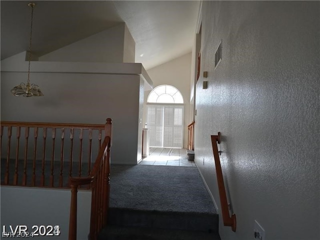 stairs with high vaulted ceiling, dark colored carpet, and a chandelier