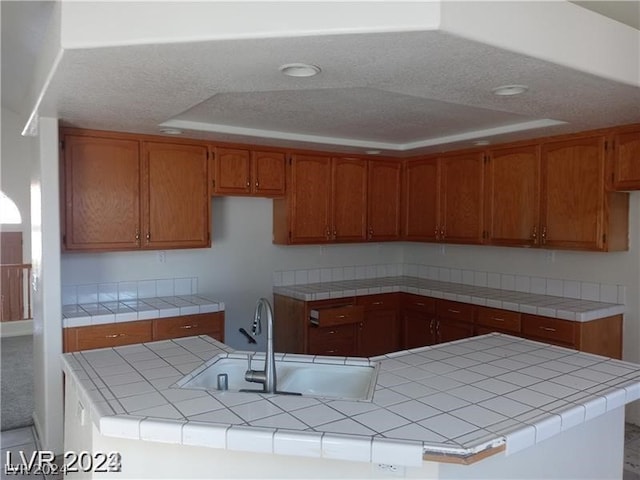 kitchen featuring tile counters, carpet floors, a tray ceiling, kitchen peninsula, and sink