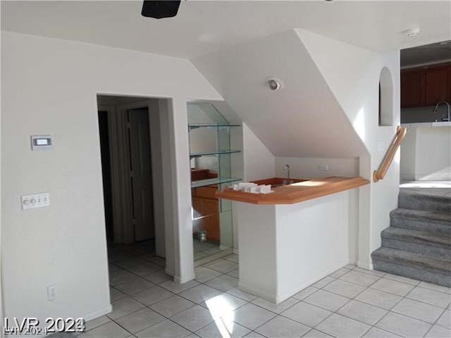 kitchen featuring kitchen peninsula, light tile floors, and lofted ceiling