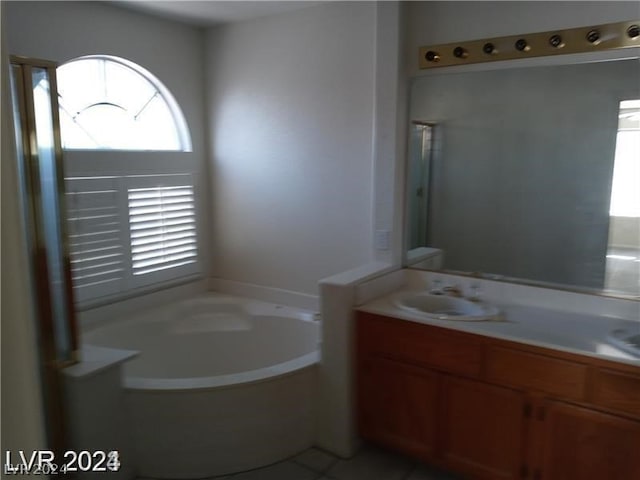 bathroom with a healthy amount of sunlight, a bath to relax in, tile flooring, and vanity