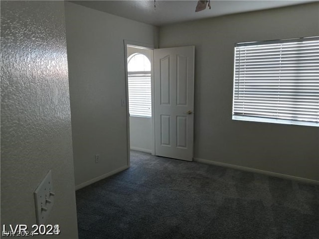 unfurnished room with dark colored carpet and ceiling fan