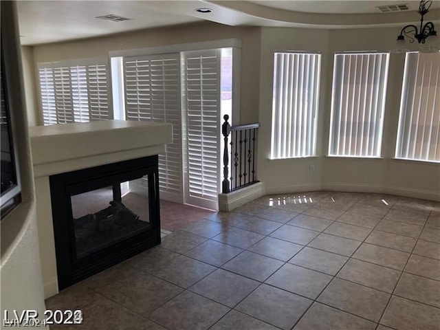 unfurnished living room with a chandelier, a wealth of natural light, and dark tile flooring