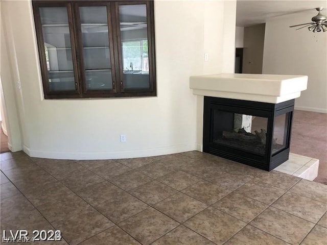 unfurnished living room featuring tile flooring, ceiling fan, and a multi sided fireplace