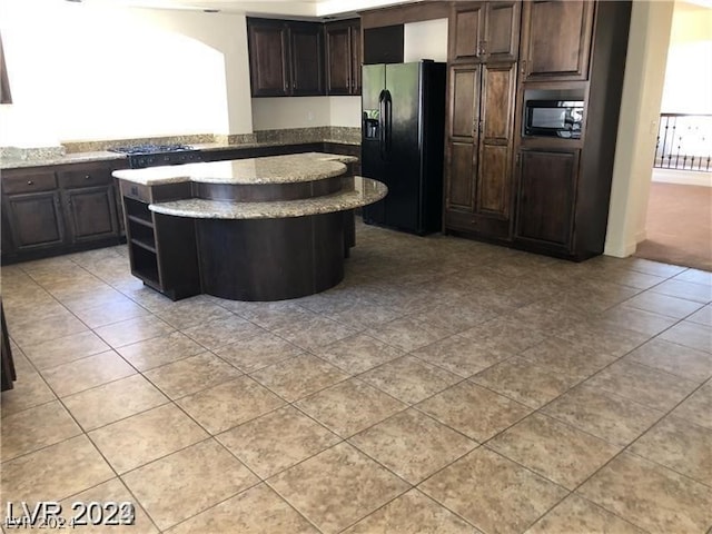 kitchen featuring light stone countertops, black appliances, dark brown cabinets, light tile floors, and a kitchen island