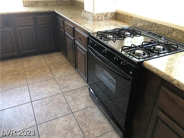 kitchen featuring dark brown cabinets, black range with gas cooktop, light tile floors, and light stone counters