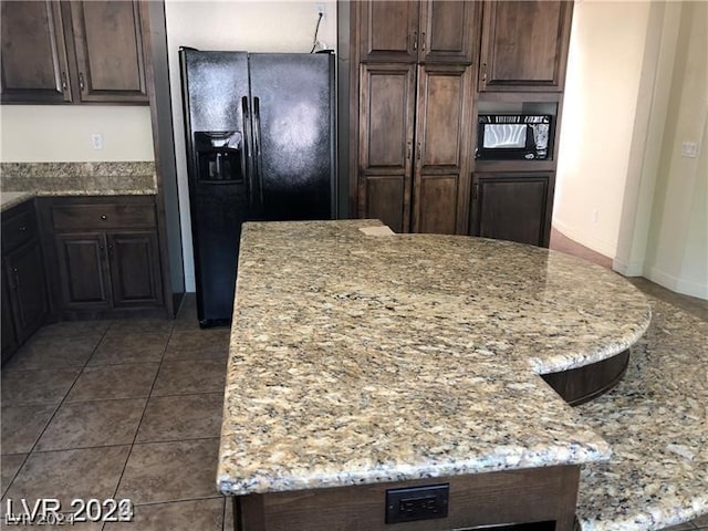 kitchen featuring dark brown cabinets, black refrigerator with ice dispenser, tile floors, and light stone countertops