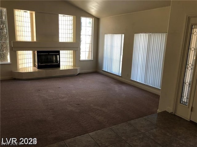 unfurnished living room with dark tile flooring, vaulted ceiling, and a tile fireplace