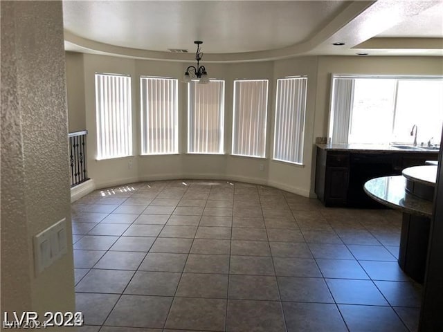 unfurnished dining area featuring an inviting chandelier, tile floors, sink, and a tray ceiling