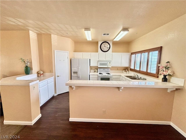 kitchen featuring a kitchen bar, sink, white appliances, and kitchen peninsula