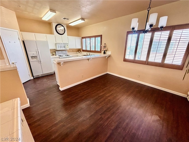 kitchen with kitchen peninsula, a notable chandelier, white appliances, white cabinets, and dark hardwood / wood-style flooring