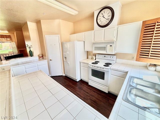 kitchen with white appliances, dark hardwood / wood-style floors, white cabinets, tile countertops, and sink