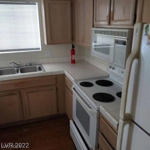 kitchen featuring dark hardwood / wood-style floors, tile counters, white appliances, and sink