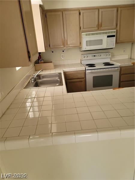 kitchen with light brown cabinetry, sink, tile counters, and white appliances