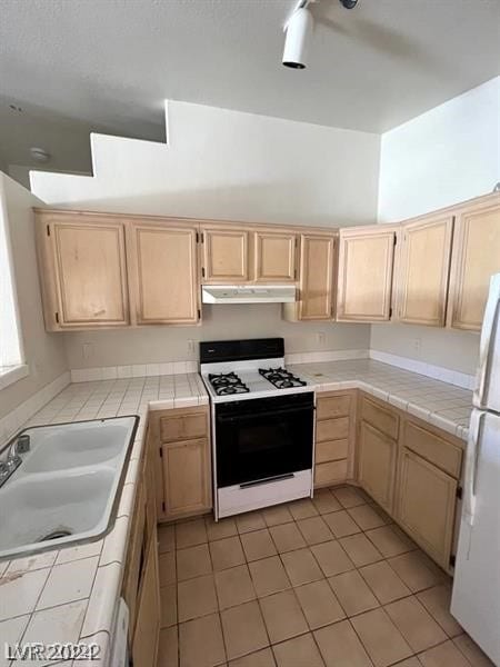 kitchen with tile countertops, white appliances, sink, and light tile floors