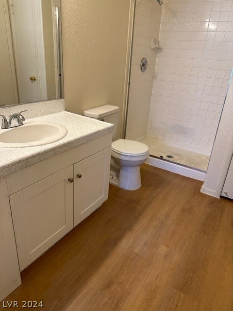 bathroom featuring tiled shower, toilet, vanity, and hardwood / wood-style floors