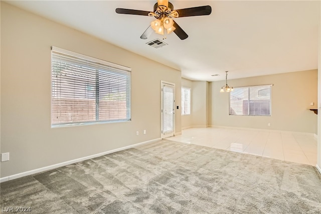 carpeted spare room featuring ceiling fan with notable chandelier