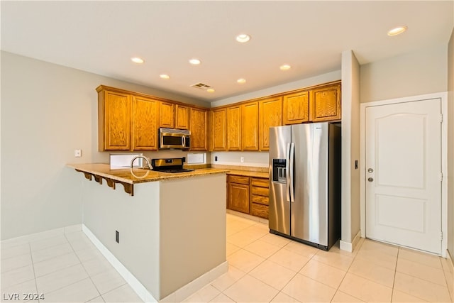 kitchen featuring kitchen peninsula, stainless steel appliances, light stone counters, light tile floors, and sink