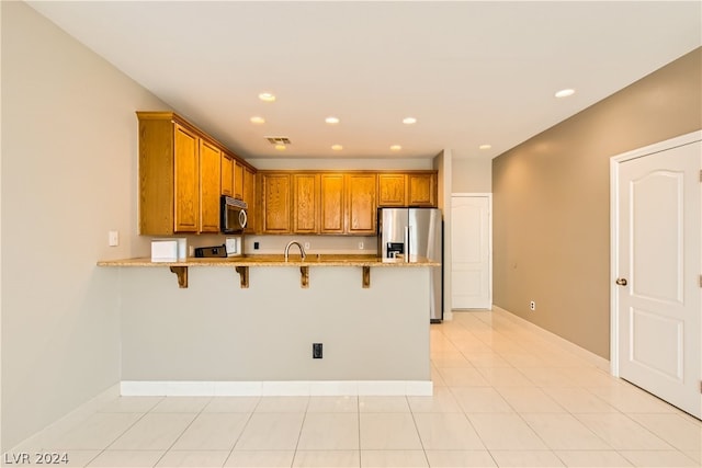 kitchen with light stone counters, light tile flooring, kitchen peninsula, appliances with stainless steel finishes, and a breakfast bar