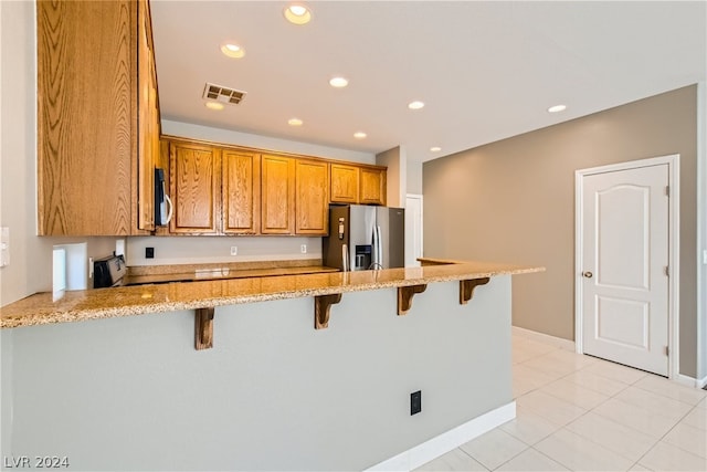 kitchen featuring light stone countertops, a breakfast bar area, light tile flooring, and stainless steel refrigerator with ice dispenser