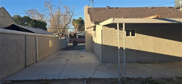 view of home's exterior with a shingled roof, a patio area, fence, and stucco siding