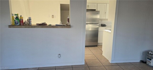 kitchen featuring light tile patterned floors, baseboards, freestanding refrigerator, light countertops, and white cabinetry