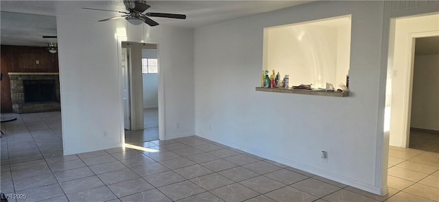 empty room with ceiling fan, light tile patterned floors, a fireplace, and baseboards