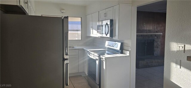 kitchen with a fireplace, white cabinetry, stainless steel appliances, and light countertops