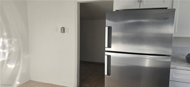 kitchen featuring light tile patterned floors, light stone counters, white cabinetry, baseboards, and freestanding refrigerator