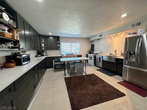 kitchen with a textured ceiling, stainless steel appliances, light tile floors, and sink