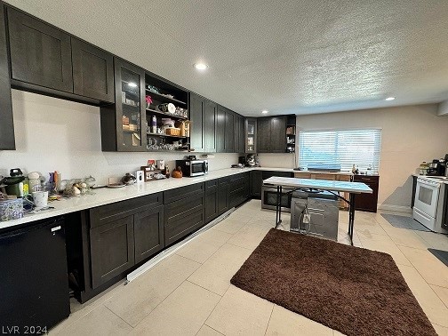 kitchen featuring a textured ceiling, white stove, dark brown cabinets, and light tile floors