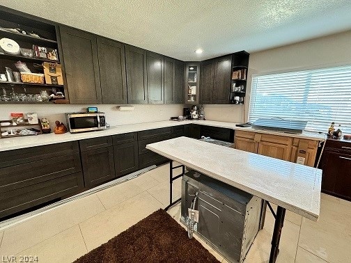 kitchen with a textured ceiling, dark brown cabinets, and light tile floors