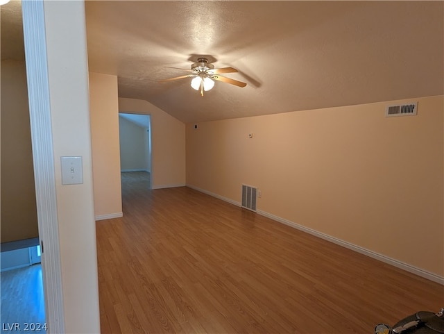 additional living space featuring hardwood / wood-style floors, lofted ceiling, ceiling fan, and a textured ceiling