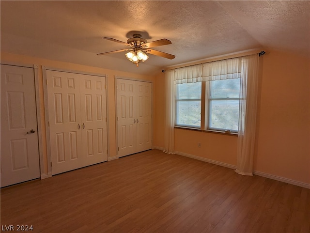 unfurnished bedroom with light hardwood / wood-style flooring, multiple closets, ceiling fan, a textured ceiling, and lofted ceiling