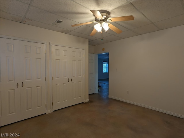 unfurnished bedroom with ceiling fan, dark colored carpet, two closets, and a paneled ceiling