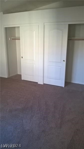 unfurnished bedroom with dark colored carpet and two closets